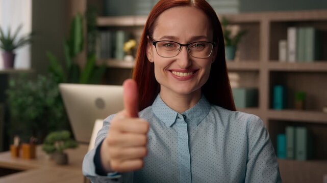 Smiling joyful Caucasian business woman wearing eyeglasses showing thumb up in office happy female manager approval gesturing recommendation support businesswoman confident girl success result inside