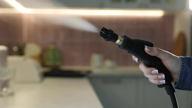 Woman with steam cleaner in kitchen, closeup. Camera moving forward and backwards