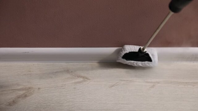Woman cleaning baseboard with steam cleaner near brown wall indoors, above view
