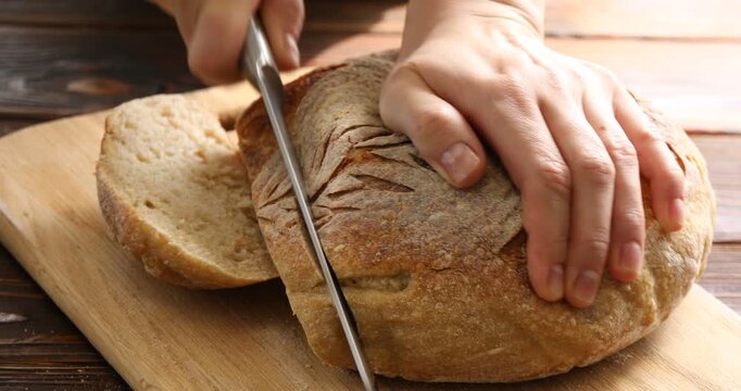 Woman cutting freshly baked bread at wooden table, closeup