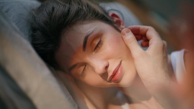 Woman lying pillows sunny portrait. Unknown man caressing sleepy girlfriend face