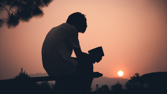Human holding Bible and praying with light sunset background, christian silhouette concept.