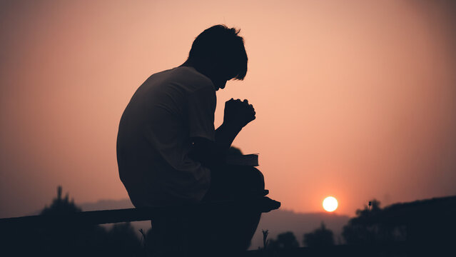 Human praying with light sunset background, christian silhouette concept.