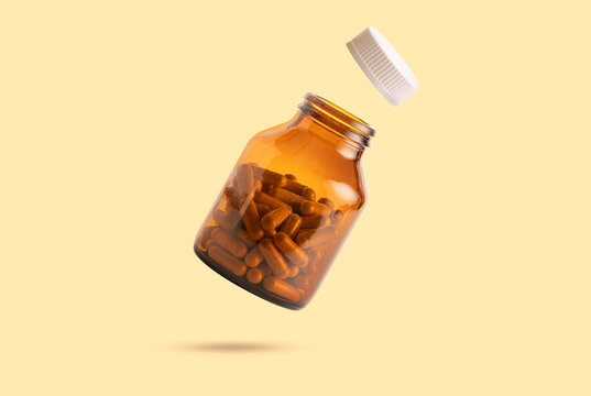 Creative shot of amber glass supplement bottle and white cap floating in the air.  for herbal medicine, vitamins, and healthcare products on soft yellow background.