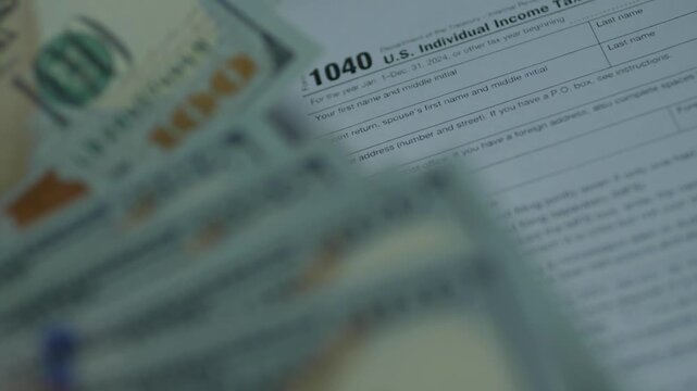 Hundred dollar bills falling on US Individual Income Tax Return form 1040. Concept of government taxation, cash refund and year-end financial reporting