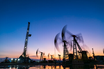Obraz premium in the evening, oil pumps are running, The oil pump and the beautiful sunset reflected in the water, the silhouette of the beam pumping unit in the evening.
