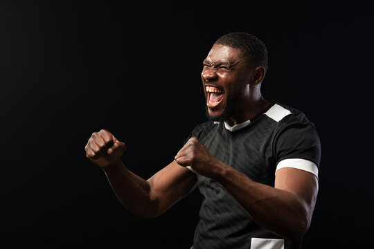 Mid-adult African man shouting, clenching fists and sweating in studio, black shirt with white trim