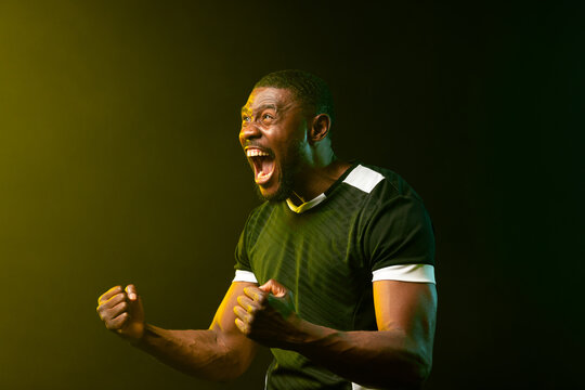 Mid-adult African man shouting and clenching fists in studio in dark green jersey with white trim