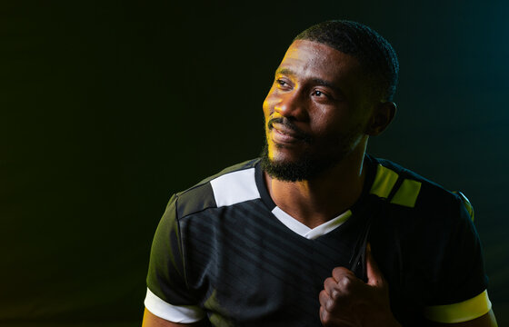 Mid adult African man gazing up-left in black sport jersey with white-yellow accents in studio