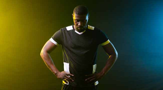 African American man posing in studio wearing dark jersey and shorts, lit by green, blue gels