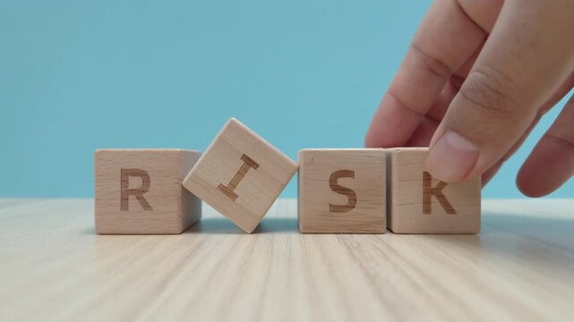 Close-up of a person's hand placing a wooden block to complete the word RISK on a wooden table. Concept of risk management, business strategy, and financial uncertainty