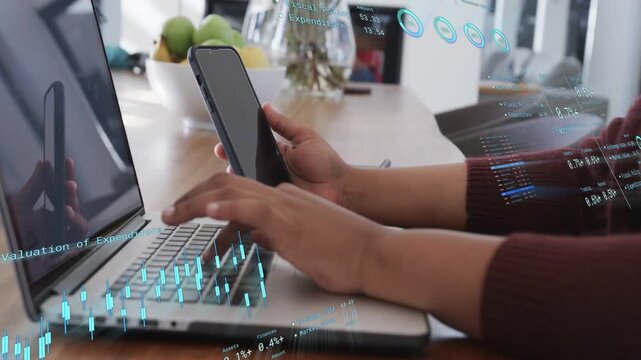 Holding smartphone and typing on laptop, woman causing finance charts and monitoring funds