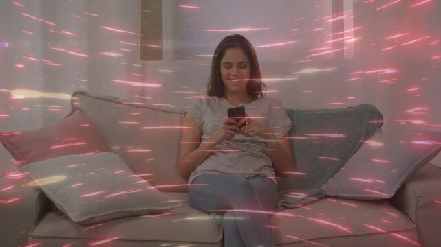 Woman tapping phone on sofa, browsing app content while pink streaks overlaying scene for tech demo