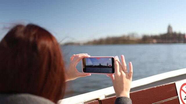 Young woman filming on smartphone while traveling on boat wind blowing hair cinematic travel lifestyle moment on open water