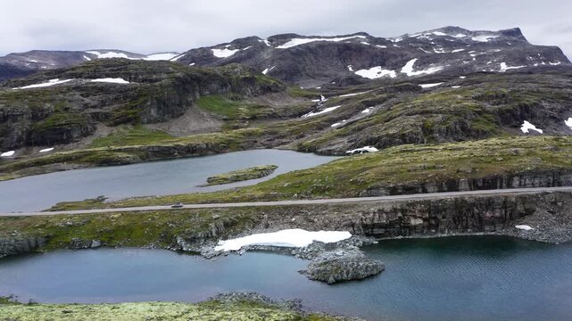 Car driving throught Norvegian severe Tundra nature with birdsyey top view Picturesque northern lakes Norwagian landscape and modern highway construction aerial 4K video. Rondane National Park, Norway