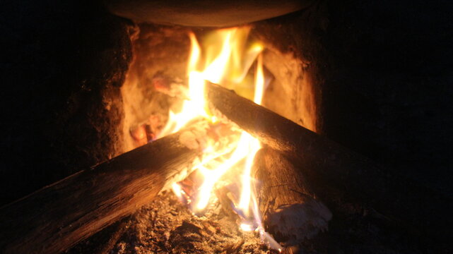 Close up of burning wood logs blazing in flames inside black wrought iron wood burning fire.
