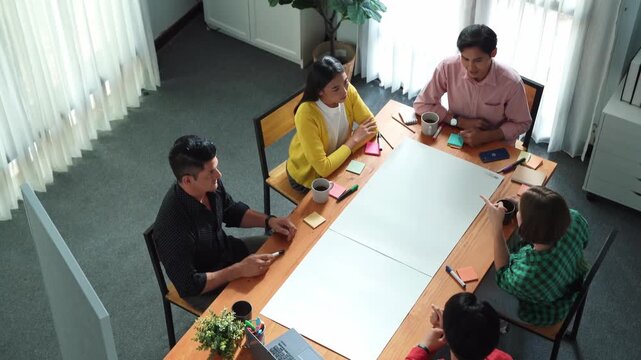 Top view of skilled manager discussing and explain strategy at meeting. Professional smart businessman standing at blackboard and sharing marketing plan while brainstorming idea at table. Convocation.