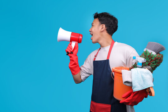 Side View of Cheerful Asian Male Cleaner Shouting Through Megaphone and Carrying Bucket of Tools