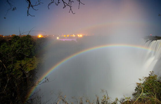 Full arc moonbow lunar rainbow over the gorge at Victoria Falls at night with illuminated bridge in background, shot from Zambia &ndash; UNESCO World Heritage Site, Africa