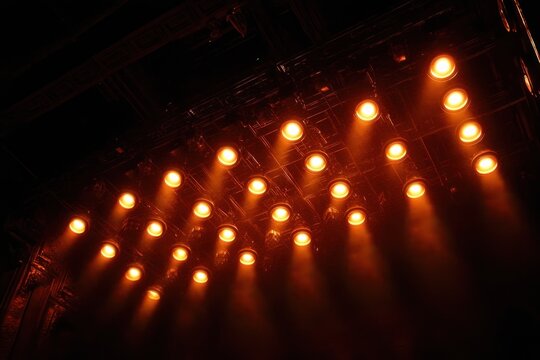Warm orange stage spotlights in grid on ceiling rig casting dramatic beams through haze in a dark theater