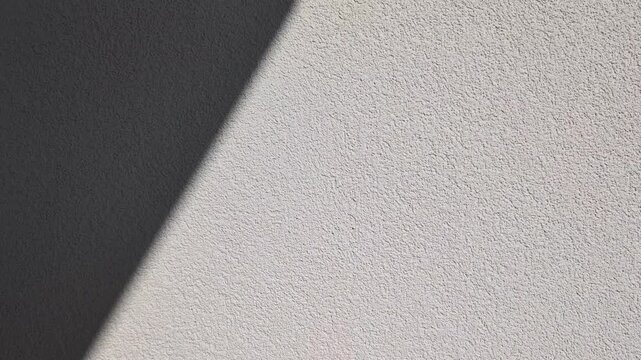 Horizontal wall texture with diagonal sunlight shadow, minimalist plaster surface, grainy cement backdrop, candid style video, architectural detail, abstract light and shadow, cinematic static shot.