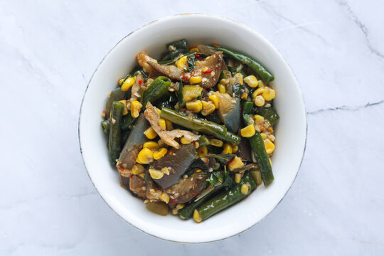Top view of a bowl of Sayur Rica Rodo, a traditional Manadonese vegetable dish from North Sulawesi. It consists of sauteed eggplant, corn kernels, long beans, and shredded fish.