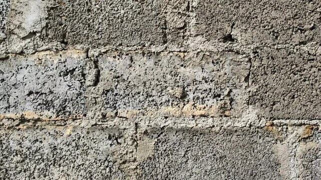 Cinder block wall texture, concrete brick surface, gray masonry construction background, candid style video, industrial building material, rough cement blocks detail, architectural backdrop. 