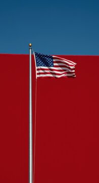 Red background and blue sky with an American flag waving on a tall silver pole for patriotic holiday marketing, national celebration banners and political design