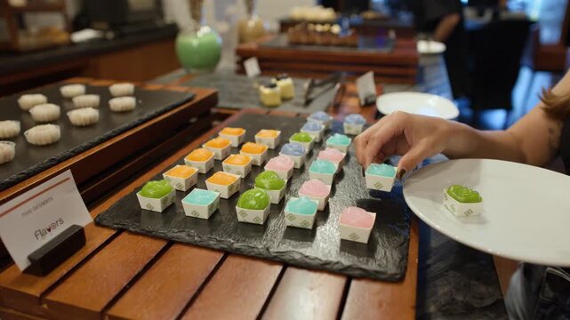 Person Picking Colorful Thai Jelly Desserts from a Buffet Display