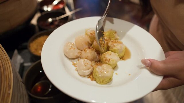 Person Sprinkling Fried Garlic Over Steamed Shumai Dumplings at Buffet
