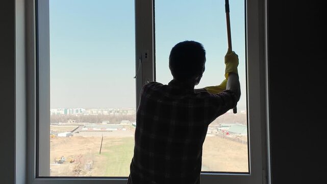 Silhouette of a professional cleaner using a squeegee to wash a large window. Housekeeping service worker doing domestic chores at home