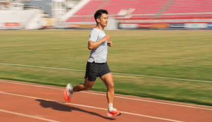 Fototapeta premium A focused athlete sprints on an outdoor track stadium seating blurred in background