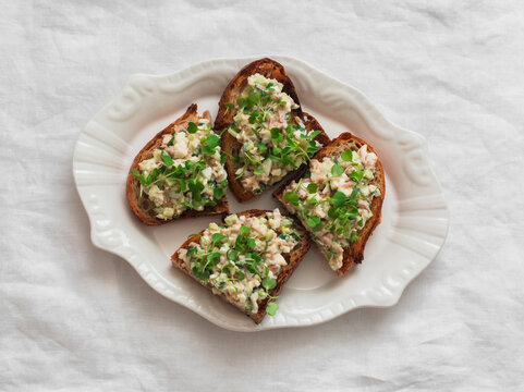 Tartine bread sandwich with canned tuna, eggs, cucumber salad on a light background, top view