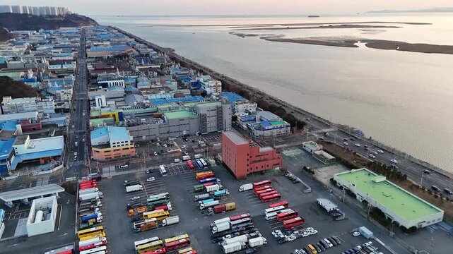 Drone aerial footage of coastal city industrial area truck parking road along sea river shoreline urbanization environmental concept South Korea