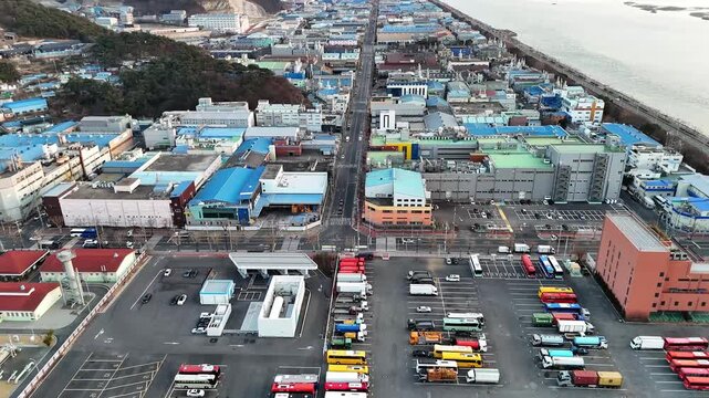 Drone aerial footage of industrial coastal city bus and truck parking road along sea dense buildings urbanization environmental concept South Korea