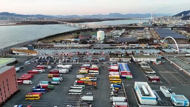 Drone aerial footage of bus and truck parking near river and sea industrial coastal area road bridge urbanization environmental concept cityscape South Korea