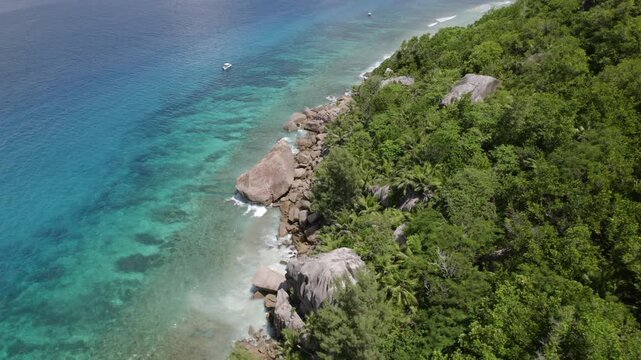 Aerial flight from lush granite mountains of Little Sister Island to a pristine white sand beach and turquoise ocean with anchored boats in Seychelles. 003 30fps