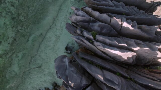 Backward drone Stunning top-down reveal of unique fluted granite rock formations meeting crystal clear turquoise waters and coral reefs at Anse Grosse Roche, La Digue, Seychelles. 015 30fps