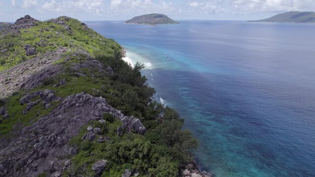 Aerial descent from lush granite peaks of Petite Soeur Island to a pristine white sand beach and crystal-clear coral reefs with boats anchored in the turquoise Indian Ocean 006 30fps