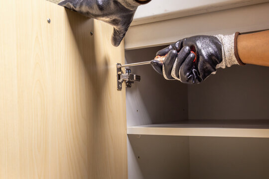 Handyman fixing cabinet door hinge on kitchen cabinet.
