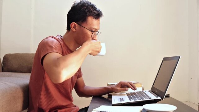 asian man drink a cup of coffe when working on laptop