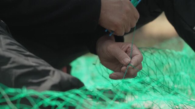 Skillful hands mending and weaving a fishing net with a needle