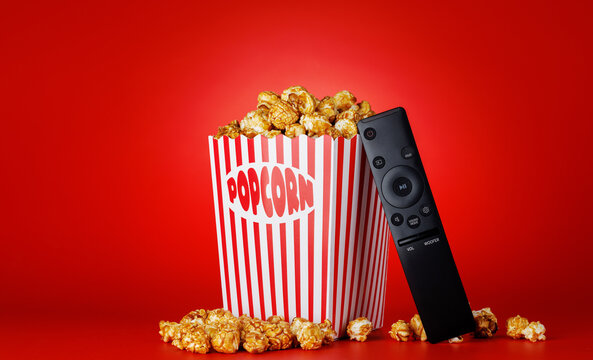 Popcorn and TV remote on red background