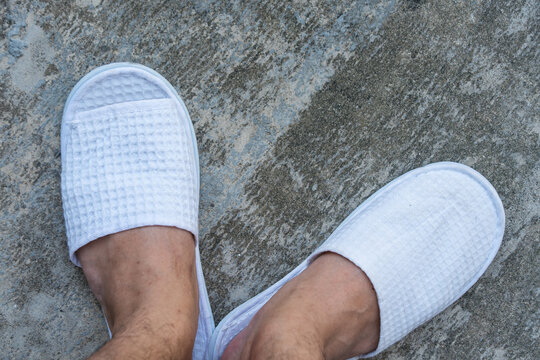 Man in feet in white slippers walks on the cement ground. Top view