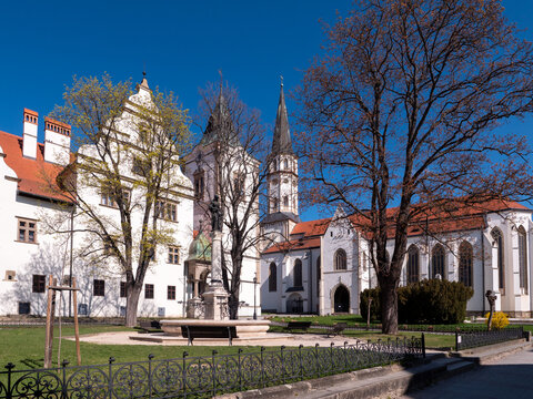 Historic square with fountain, town hall and St James Basilica in Levoca, Slovakia. UNESCO old town architecture surrounded by trees under clear blue sky.
