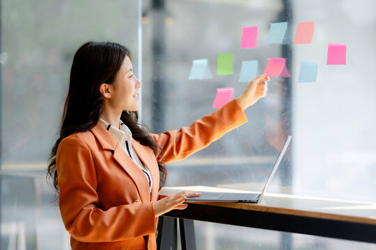 Businesswoman organizing creative ideas on a glass wall during a planning meeting, managing project tasks with agile methodology