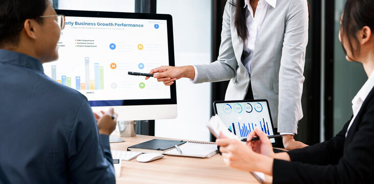Business team analyzing financial growth data on a computer screen and tablet during a professional meeting in a modern office boardroom.