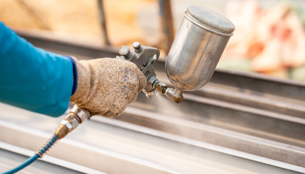 Construction worker painting metal structure surface coating with a spray gun at construction site. Metal corrosion and rust protection. Industrial precision. Protective coating to a metal structure.