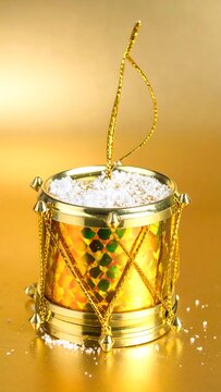 Golden, detailed drum ornament with white snow, on a bright gold backdrop