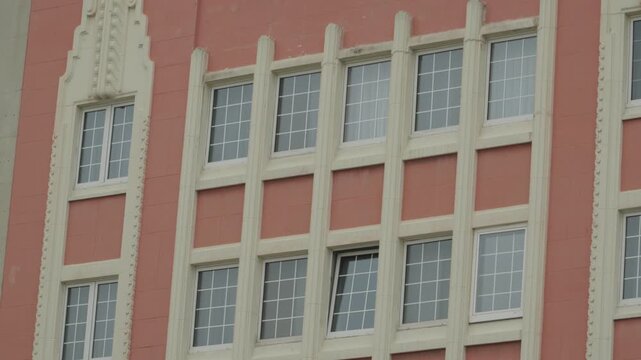 Close-up of a classic art deco building exterior in Gijon, Spain, featuring ornate white decorative columns and symmetrical grid windows on a terracotta pink facade.
